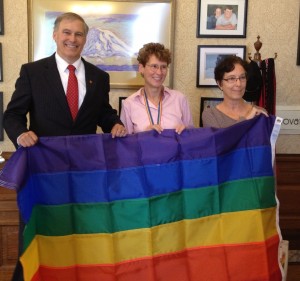 Governor Inslee receives a Rainbow Flag from Capital City Pride chair Anna Schlecht and volunteer Sarah Vanucci.