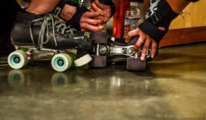 Players Naughty Mommy and Holy Eep helping each other with skates in between jams.  Photo Credit Regularman Photography