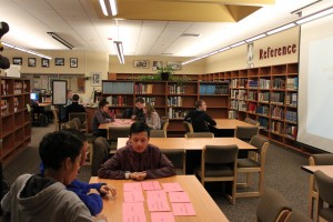 Students hold up sheets of paper with the book titles on them to give their answers. If they are correct, they are awarded a point.