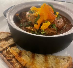 lamb stew in a black bowl with a piece of bread on the side at Cynara