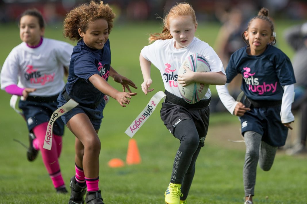 Young girl reaching for another girl's flag in rugby, while two more girls run towards them