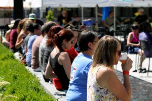 A long row of people sitting at a table outside drinking at the Lacey South Sound BBQ Festival