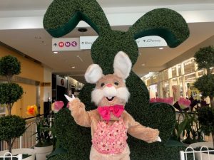A person dressed as the Easter Bunny standing behind a large bunny topiary at Capital Mall