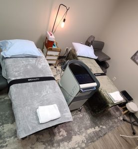 Patient room with beds and an Emsculpt machine at Rejuvenate IV Hydration & Wellness Center 