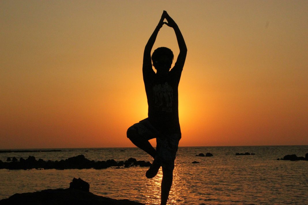 A person doing a tree yoga pose at the beach at sunset