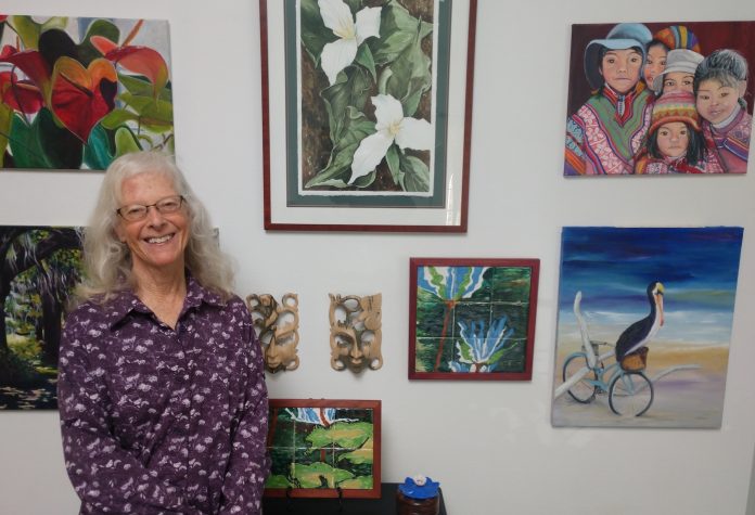 Joanne Osband stands by her art hanging on a wall in Olympia