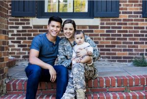 military woman with child on lap and husband sitting next to her on a brick porch of a home