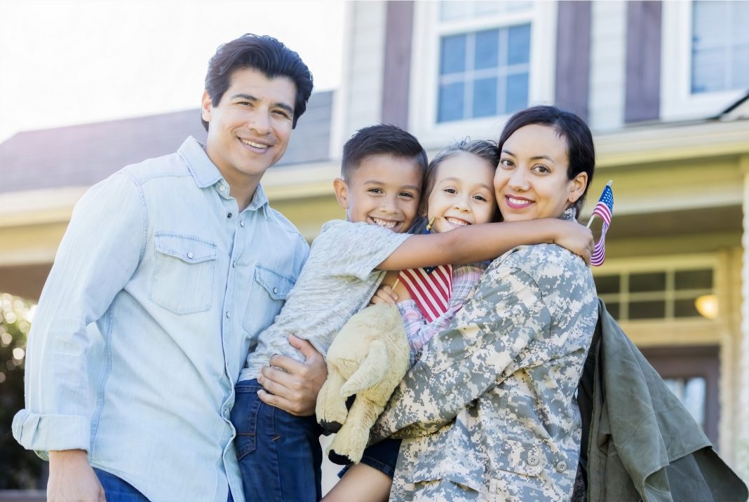 military woman hugging her two children and husband outside a home