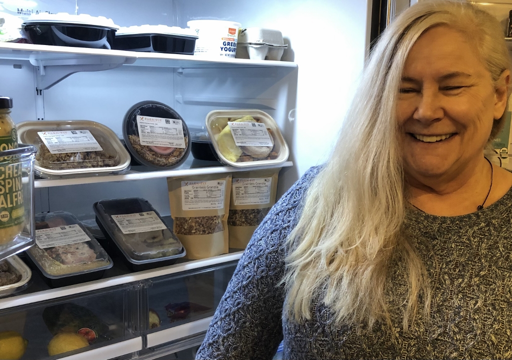 woman standing by her open fridge door that stocked with food from Farm to Fit