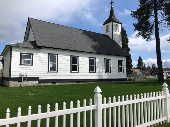 This view of Rainier's historical church from Minnesota Street showcases the freshly painted white siding, windows, gabled roof, tower and white picket fence.