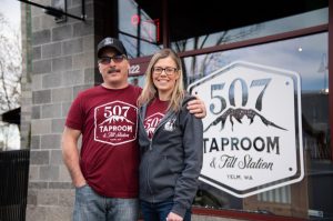 Owner Bill DeVore and a woman standing next to the 507 Taproom & Filling  Station sign