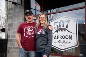 Owner Bill DeVore and a woman standing next to the 507 Taproom & Filling Station sign