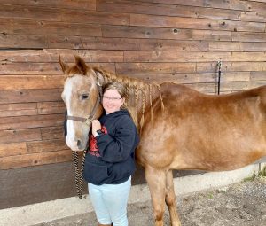 Morgan, a young girl, standing with Scout, her new horse, against a wooden wall