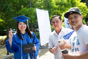 SPSCC graduate in cap and gown with two people standing next to her with signs