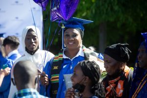 SPSCC grad in cape and gown in a group of people with balloons