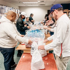 people in two lines along a table filling bags for All Kids Win