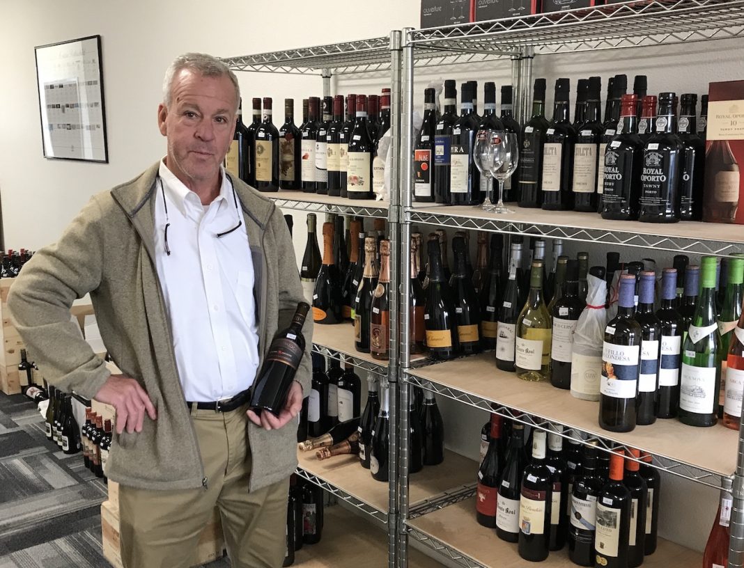 Ed Schlich a wine educator and owner of Oly Wines in Tumwater, standing buy a rack of shelves full of bottles of wine