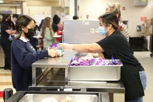 child in mask at a school cafeteria being handed food by a lady