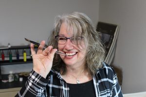 Thurston County artist Bonnie Belden-Doney  holding a paintbrush up to her mouth and smiling