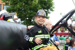 child in a fire jacket sitting behind the wheel of an emergency vehicle at Hands On Children's Museum