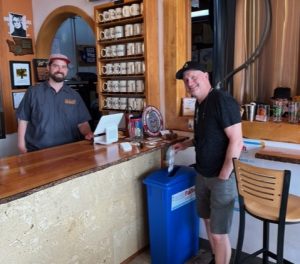 Beer tender Matthew Karas with customer Chris Sheldon who is tossing in a plastic can holder top for recycling.
