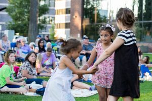 three girls holding hands in a circle on the grass in front of a crowd at Lacey In Tune