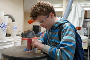 Student Alex Malone works on the sanders to finish softening the edges of an Among Us character built from wooden blocks. 