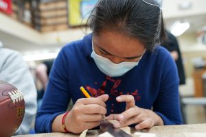 Student Shaiann Taimalie works on the layout of a wooden three-piece puzzle. She first drew the puzzle with specific measurements, then transferred the layout onto the wooden block. 