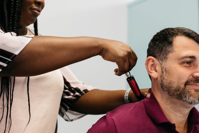 Doctor performing a chiropractic adjustment on a man sitting using an activator