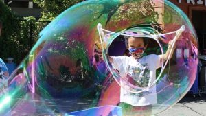 child with a huge bubble from a giant wand
