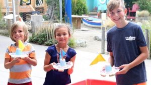 three children with toy sail boats made of recycled items the Hands On Children's Museum. 