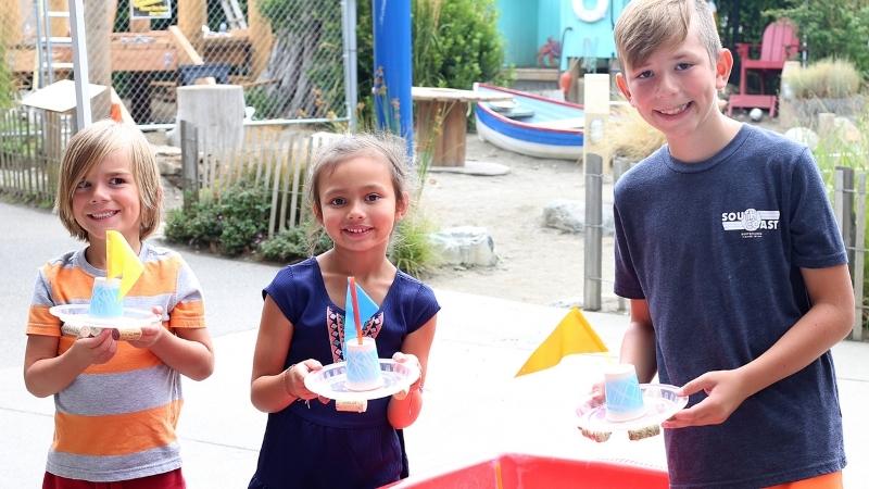 three children with toy sail boats made of recycled items the Hands On Children's Museum.
