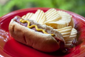 hot dog on a red plate with mustard and potato chips