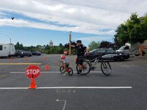 child on a bike with an officer learning bike safety at Olympia Bike Rodeo
