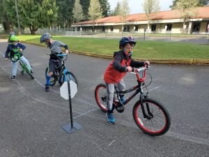 three kids on bikes stopping at a miniature stop sign at Olympia Bike Rodeo