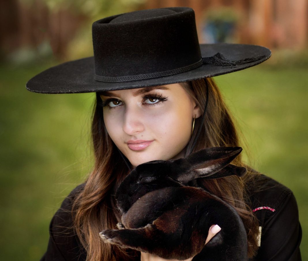 Eva C-M in a black outfit with a black hat holding a black rabbit