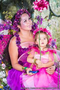 woman dressed in a purple fairy costume holding a child dressed in a pink fairy costume on her lap