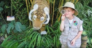 child dressed as someone on safari by a stuffed animal tiger in some foliage