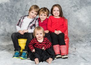 four young children pose for a professional photo, sitting down, against a grey background