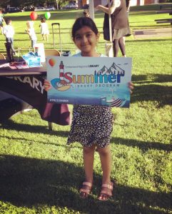 A young library patron holds a giant library card during a Summer Library Program Lacey in Tune even