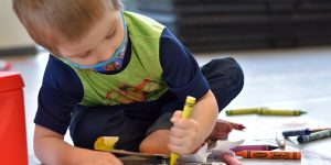 little boy with mask coloring on a page on the floor at South Sound Dance Fine Arts Club