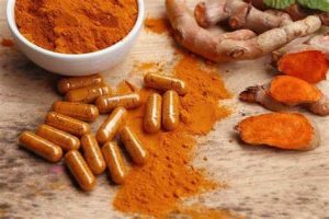 a small bowl of turmeric, with turmeric capsules next to it and loose turmeric powder and roots. 