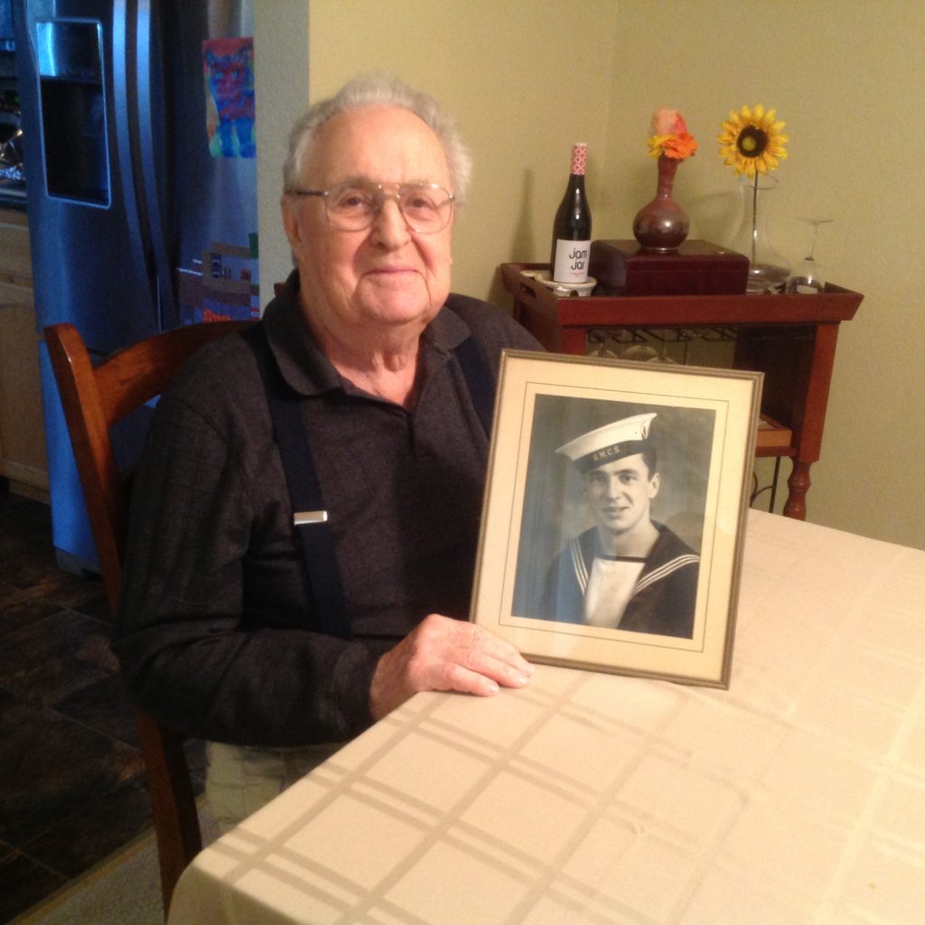 Charlie Jackman sitting at a table holding a photo of himself in Navy uniform