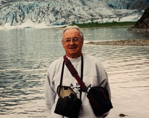 charlie standing in front of a body of water and glaciers in Alaska