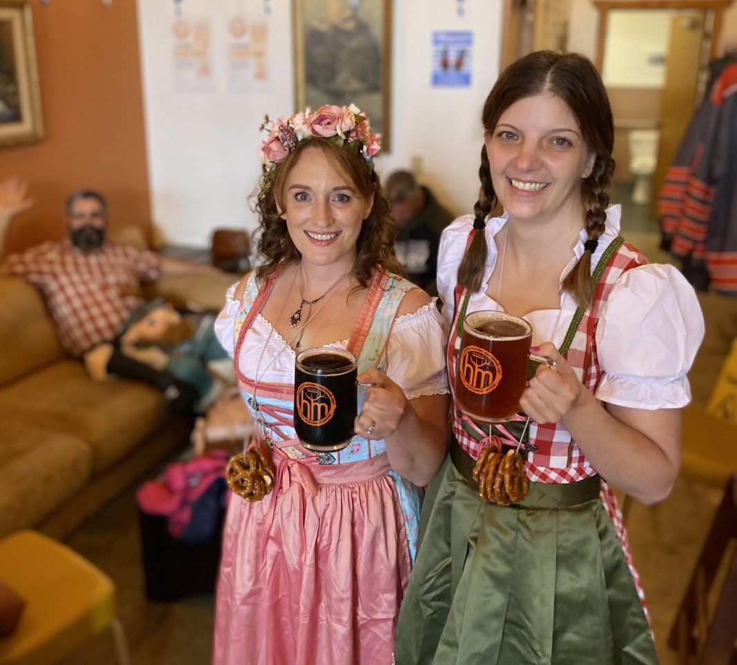 two women in German dresses hold up pints of beer at Headless Mumby