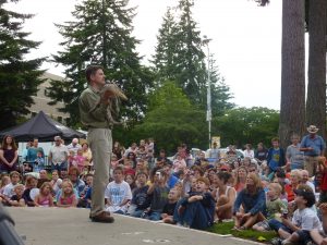 man holding a reptile on stage with a large crowd