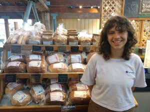 Jaina Nehm standing in front of her bread case at Olympia Farmers Market