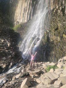 Lorraine standing with her arms outstretched below a huge waterfall