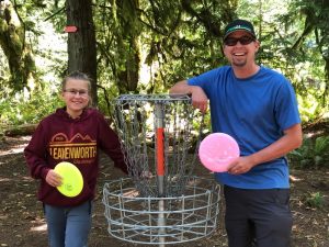 a man and child holding discs by a basket at the The Evergreen State College disc golf course