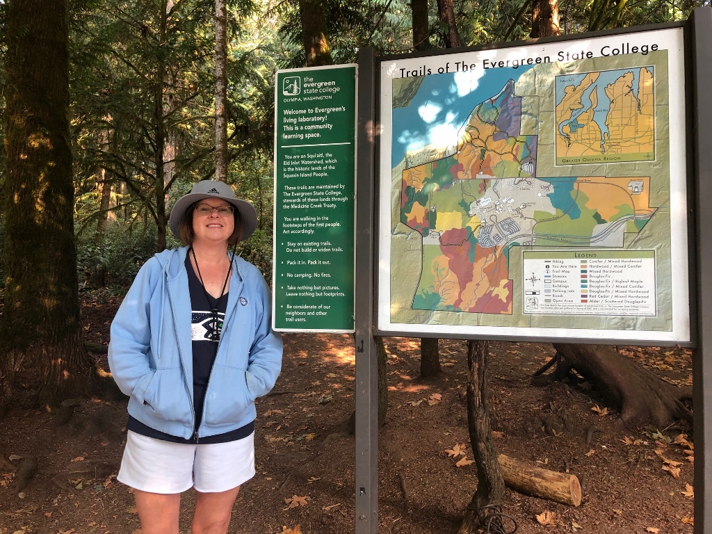 Kelly Wilson, a first-time hiker on The Evergreen State College's trails, standing next to a trail sign